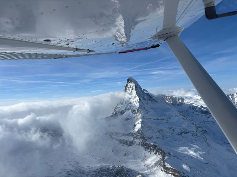 View from a plane flying over snowy mountains, with the Matterhorn peak visible through clouds.
