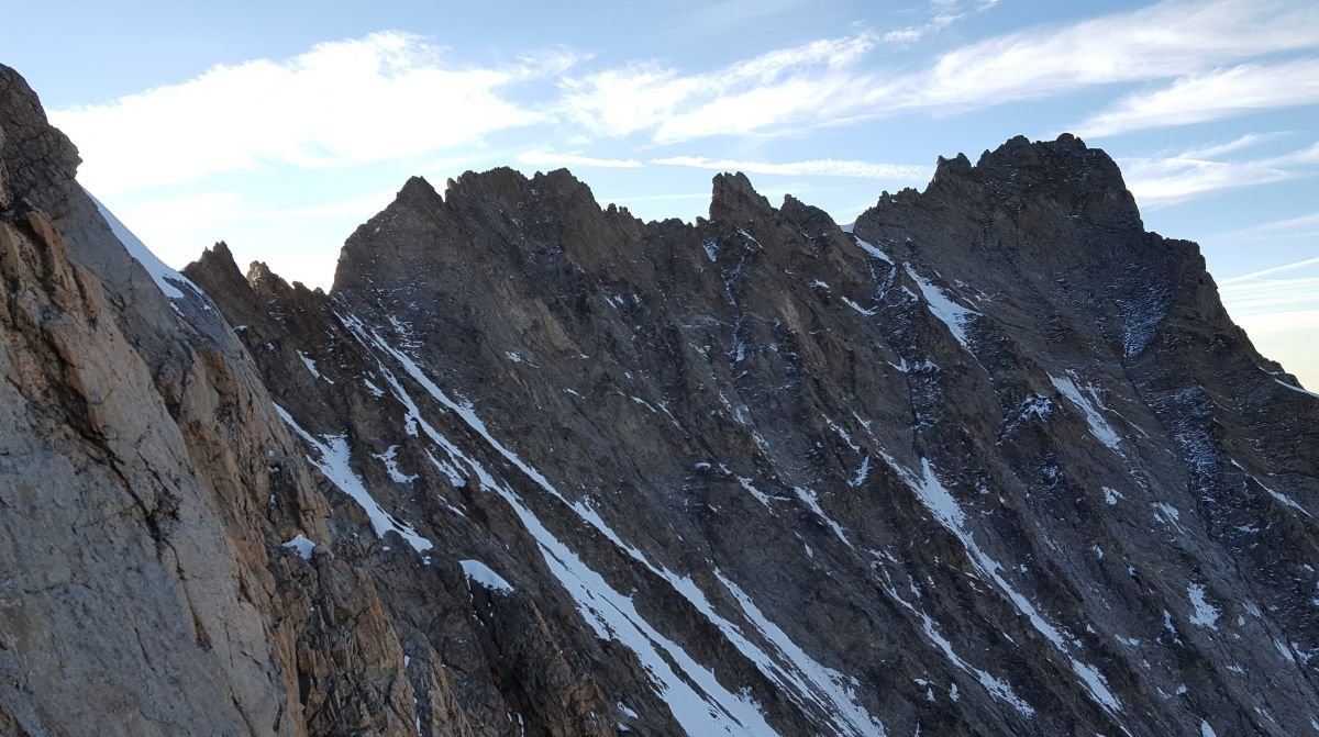 Jagged mountain peaks with patches of snow under a partly cloudy sky.