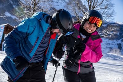 Two people with helmets and ski equipment on a snow-covered slope in the mountains.