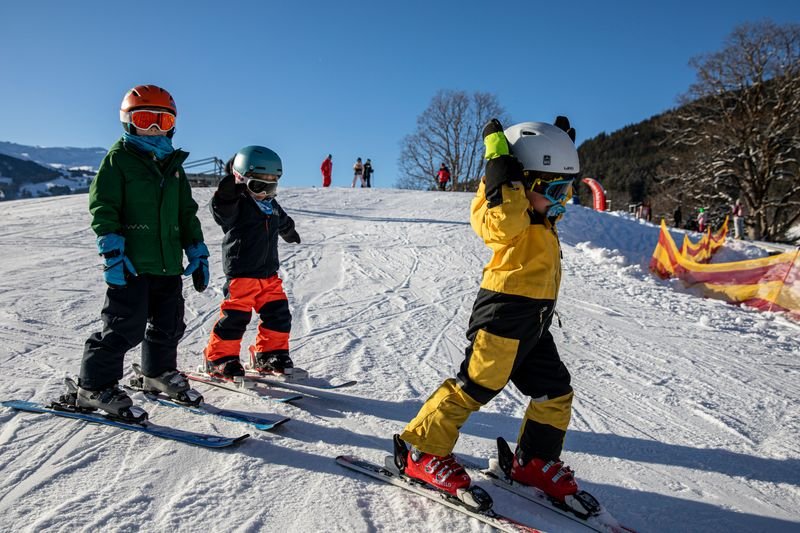 Three children with helmets and skis on a snow-covered slope in the mountains.