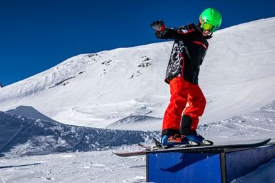 Person on snowboard with green helmet on a box in a snowy mountain area.