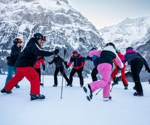 Group of people in winter gear and helmets playing on a snowy mountain slope with ski poles.