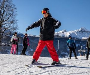 Eine Gruppe von Skifahrern auf einem verschneiten Berghang, die Helme und Skiausrüstung tragen, mit Bergen im Hintergrund.