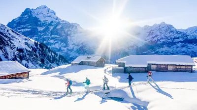Ski tourers ascending near alpine huts with the Wetterhorn in the background.
