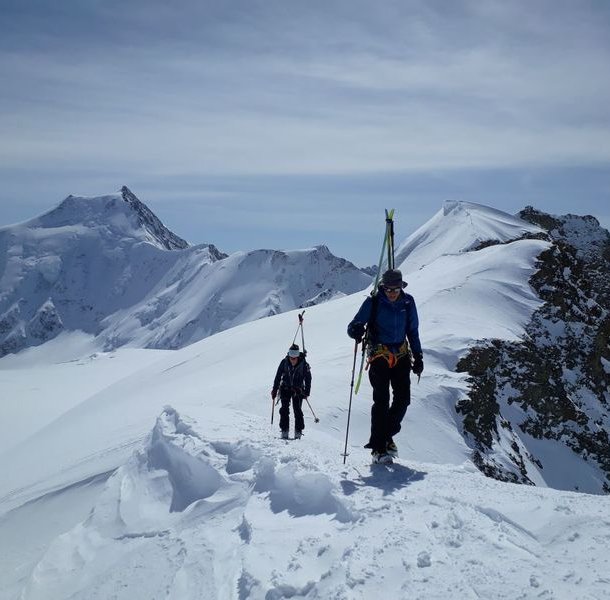 Ski tourers with skis strapped on their backs on a ridge.