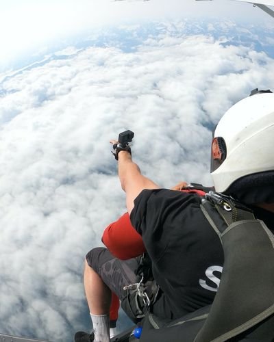 Personen mit Helmen und Fallschirmen in einem Flugzeug über Wolken.