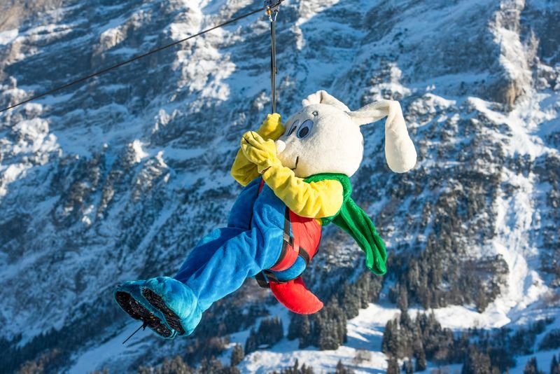 Person in rabbit costume on a zip line in a snowy mountain landscape.