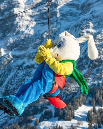Person in rabbit costume on a zip line in a snowy mountain landscape.