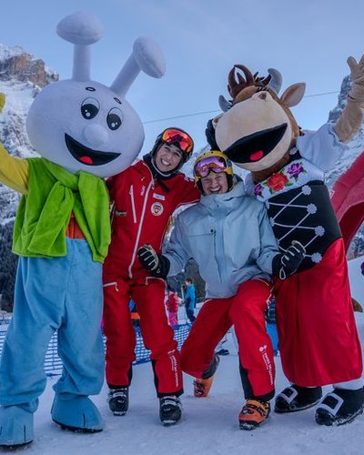 People in ski gear posing with two mascots in front of a mountain backdrop in the snow.