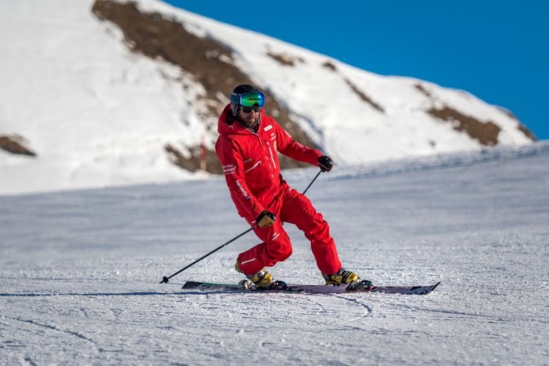 Skier in red suit with helmet and ski goggles on snow-covered mountain.