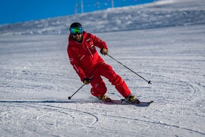 Skier in a red suit with a helmet and ski goggles skiing downhill on a snowy slope.