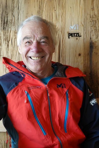 Mann mit roter Millet Jacke lächelt in die Kamera.