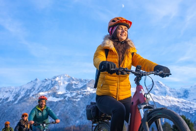 People biking with helmets and winter jackets in a snowy mountain landscape.