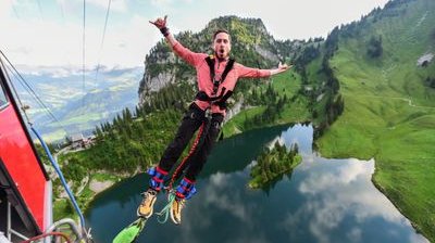 Person bungee jumping over a lake, wearing a safety harness, mountains in the background.
