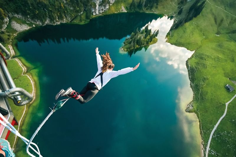 Person bungee jumping over a alpine lake, wearing a harness and ankle straps, surrounded by mountains.