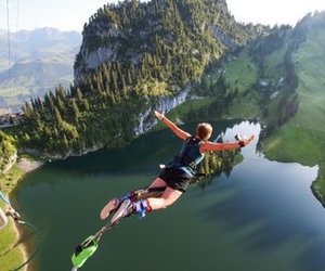Person beim Bungy Springen über einem Bergsee bei Sonnenuntergang mit weit ausgestreckten Armen