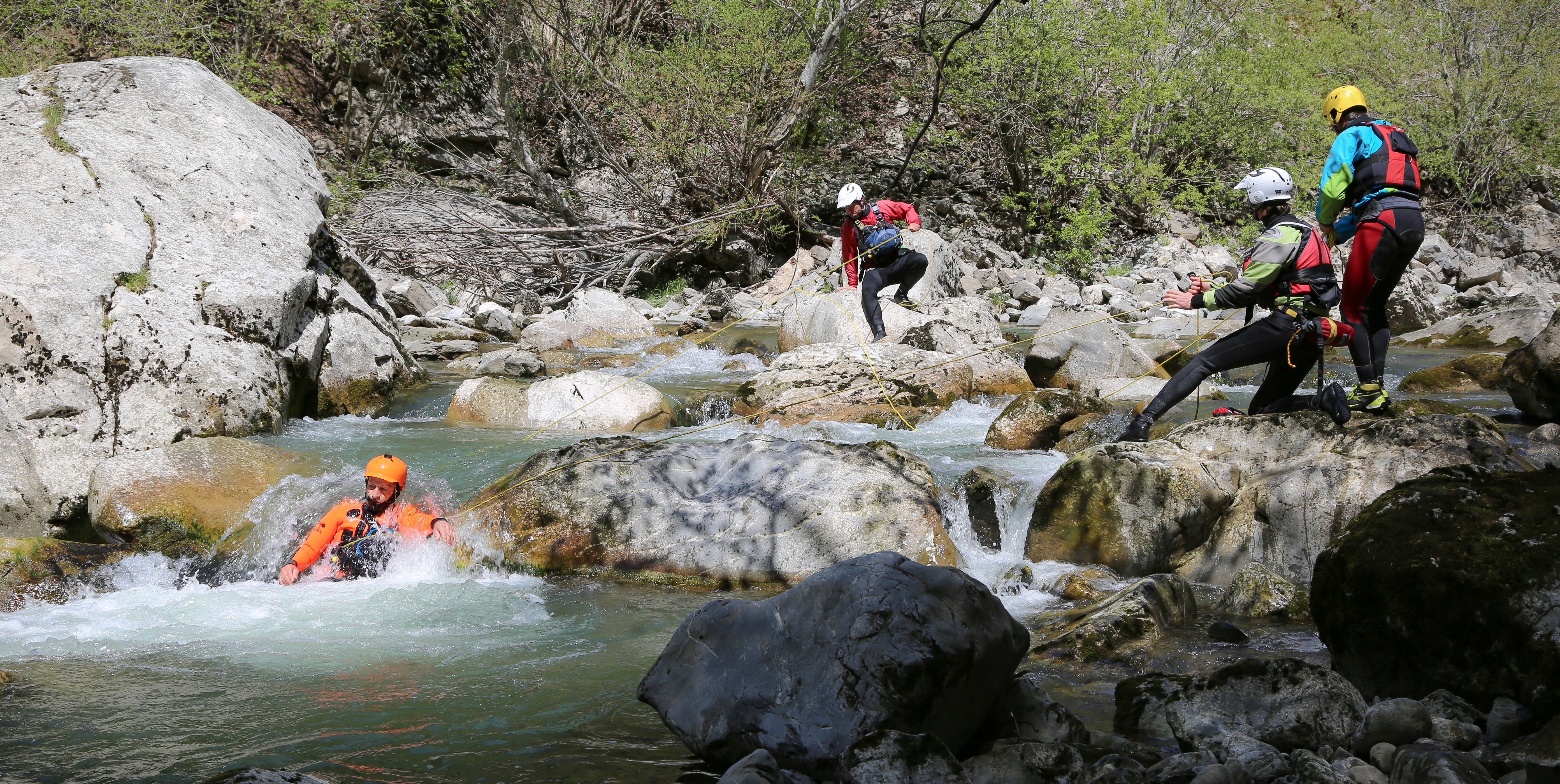 Personen mit Helmen und Neoprenanzügen beim Canyoning in einem felsigen Flussbett in den Bergen.