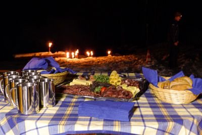 Table with food and drinks outdoors, surrounded by torches in the snow at night.