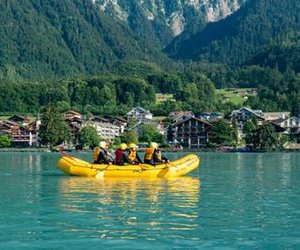Gruppe beim Family Rafting auf dem türkisblauen Brienzersee, malerisches Dorf und Berge im Hintergrund.