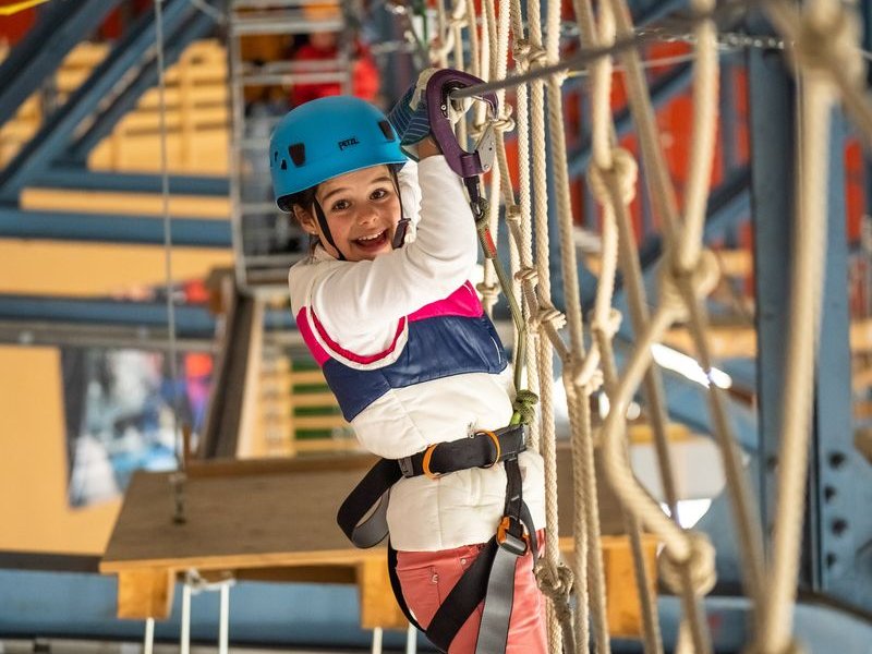 Ein Kind mit Helm und Sicherheitsgurt navigiert einen Seilparcours im Indoor Seilpark Grindelwald
