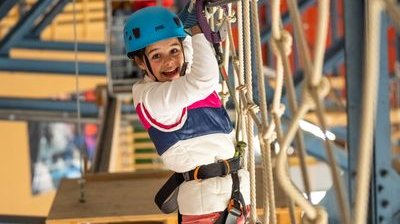 A child wearing a helmet and safety harness navigates a rope course at the Indoor Rope Park Grindelwald