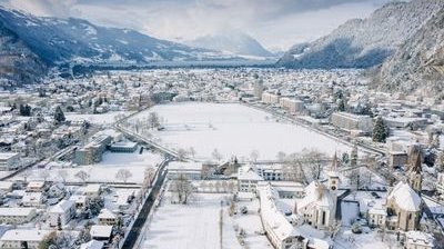 Verschneite Stadtansicht mit Bergen im Hintergrund, Gebäude und Straßen bedeckt von Schnee.