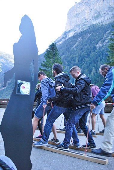 Group of people on wooden skis with poles, in the background mountains and trees.