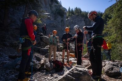 People with helmets and climbing harnesses are standing in a rocky mountain landscape and preparing ropes.