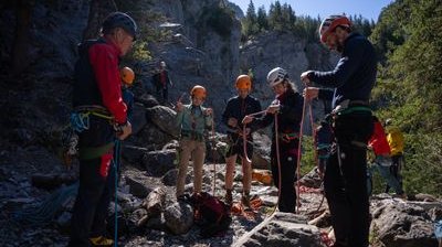People with helmets and climbing harnesses are standing in a rocky mountain landscape and preparing ropes.