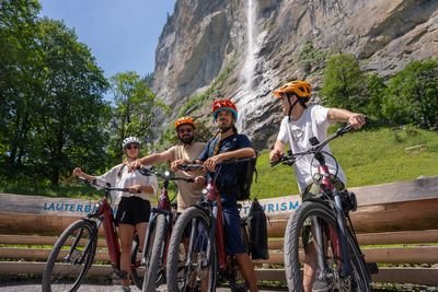 People with helmets and bicycles in front of a steep rock face.