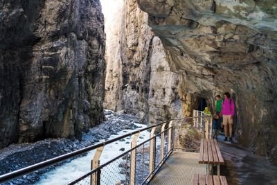Personen auf einem Steg in einer Schlucht, umgeben von Felsen und einem fließenden Bach.