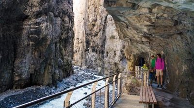 Personen auf einem Steg in einer Schlucht, umgeben von Felsen und einem fließenden Bach.