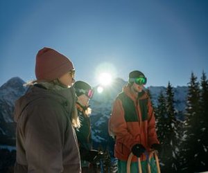 Three people in winter gear with sleds, wearing goggles and hats, in a snowy mountain setting.