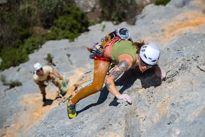 헬멧과 하네스를 착용한 두 명의 등반가가 초록으로 둘러싸인 바위 절벽을 오르고 있습니다.
