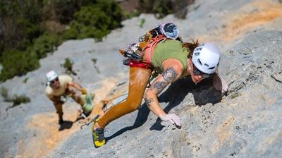 헬멧과 하네스를 착용한 두 명의 등반가가 초록으로 둘러싸인 바위 절벽을 오르고 있습니다.