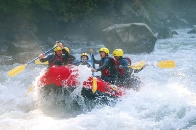 River-Rafting im Wildwasser auf der Lütschine. Teilnehmer tragen Schwimmweste und sitzen paddelnd in einem roten Schlauchboot