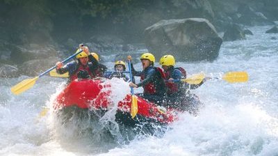 River rafting in whitewater on the Lütschine. Participants wear life jackets and sit paddling in a red raft