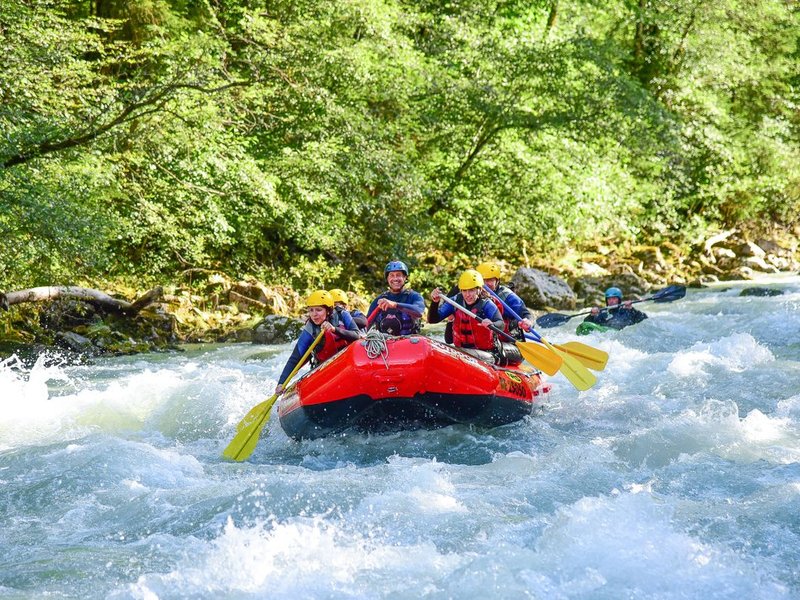 Group rafting on the Simme in the forest, with helmets and life jackets, paddling in a red inflatable boat.
