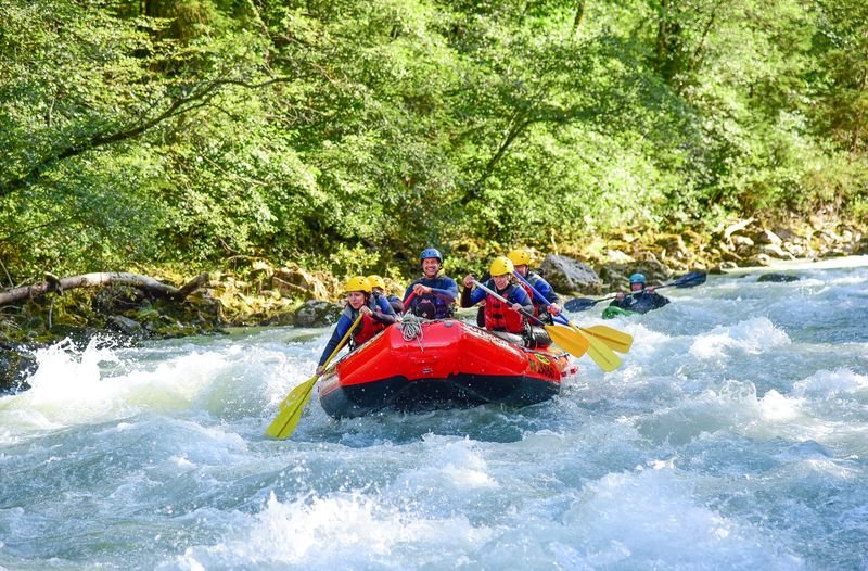 Gruppen-Rafting auf der Simme im Wald, mit Helmen und Rettungswesten, paddelnd in einem roten Schlauchboot.
