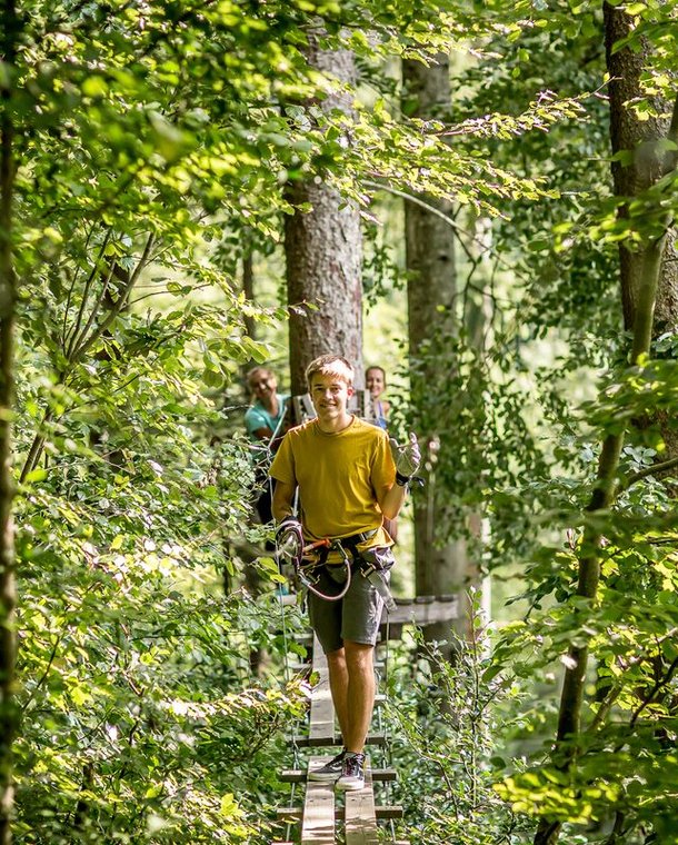 Person walks on a narrow wooden bridge in the Interlaken Rope Park through the green treetops