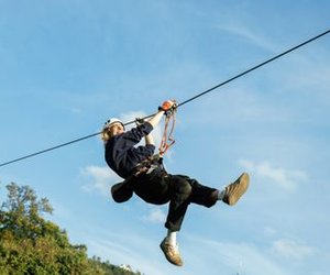 Person zip lining with helmet and safety harness in front of a blue sky.