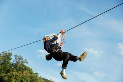 Person zip lining with helmet and safety harness in front of a blue sky.