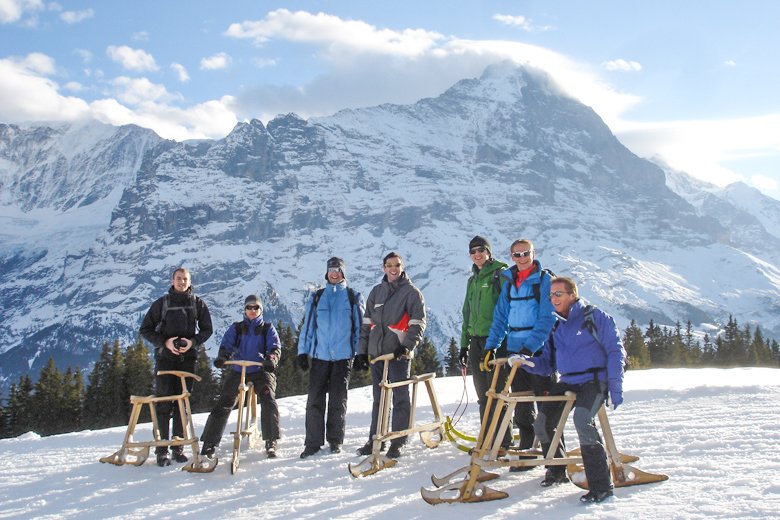 A group of people with sledges on a snow-covered mountain in an alpine setting.