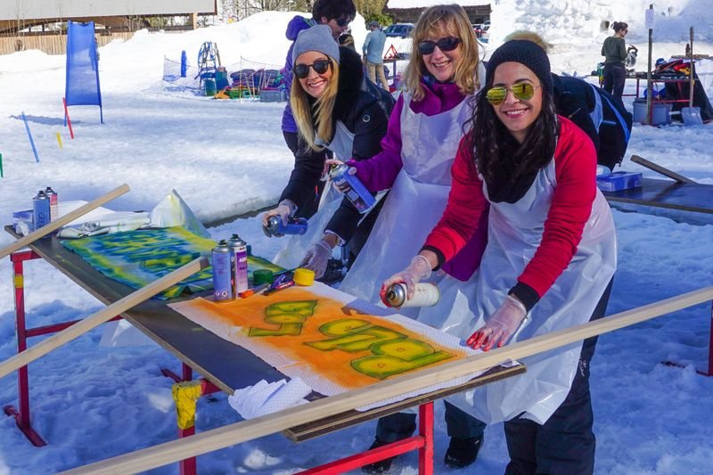 Three people are spraying graffiti on wooden boards in the snow, wearing aprons and gloves.