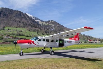 A red and white airplane is standing on a runway in front of a mountain landscape.