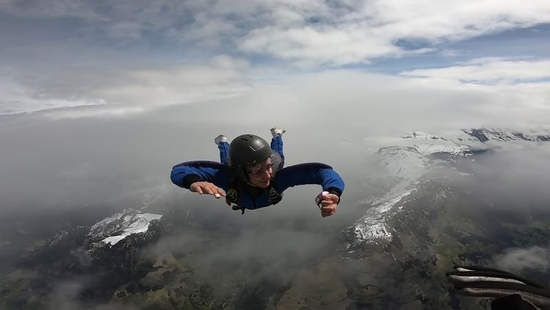 Person in a blue suit and helmet skydiving over snow-covered mountains.
