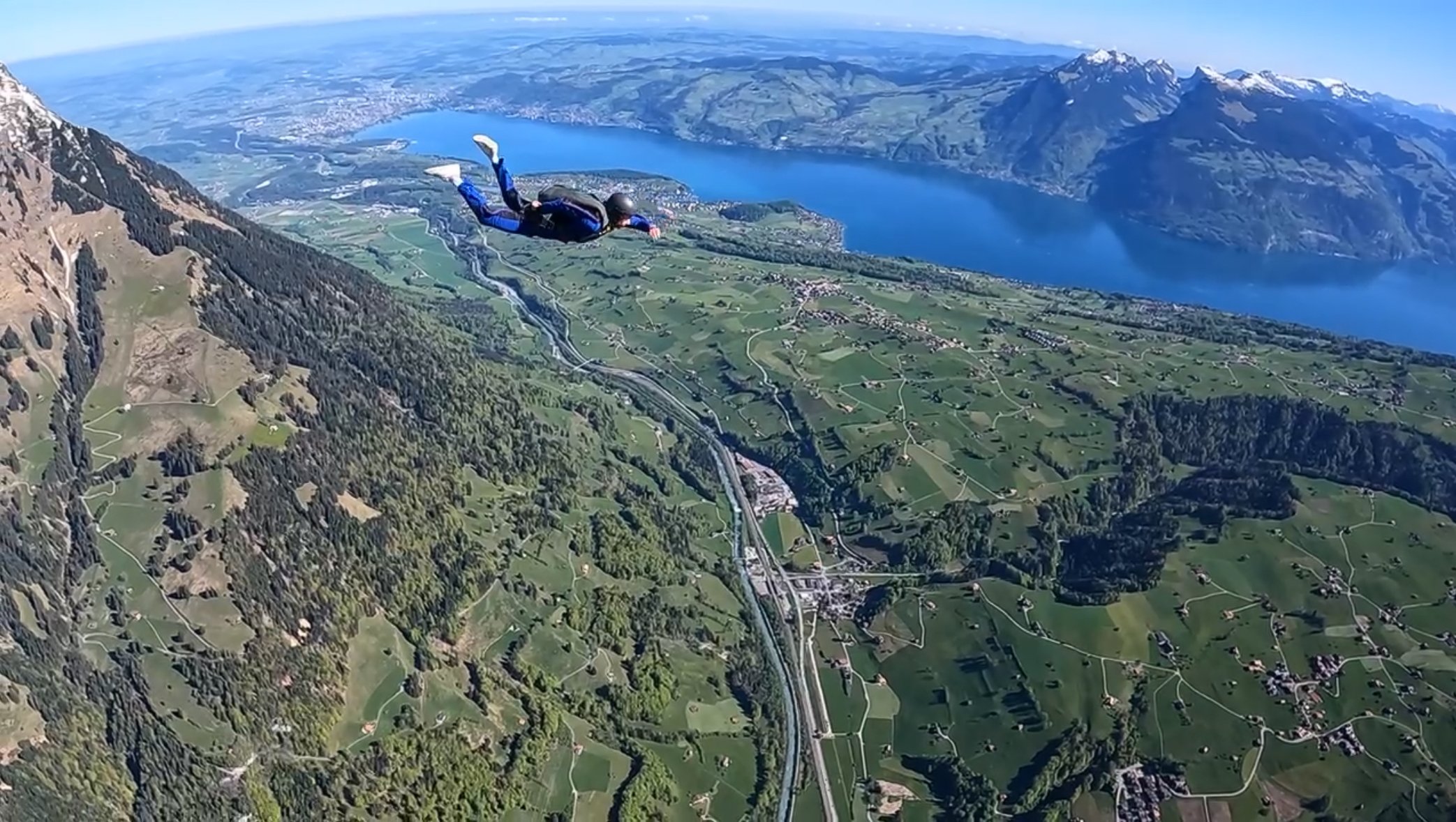 Skydiver with suit and helmet over green mountain landscape and lake in Switzerland.