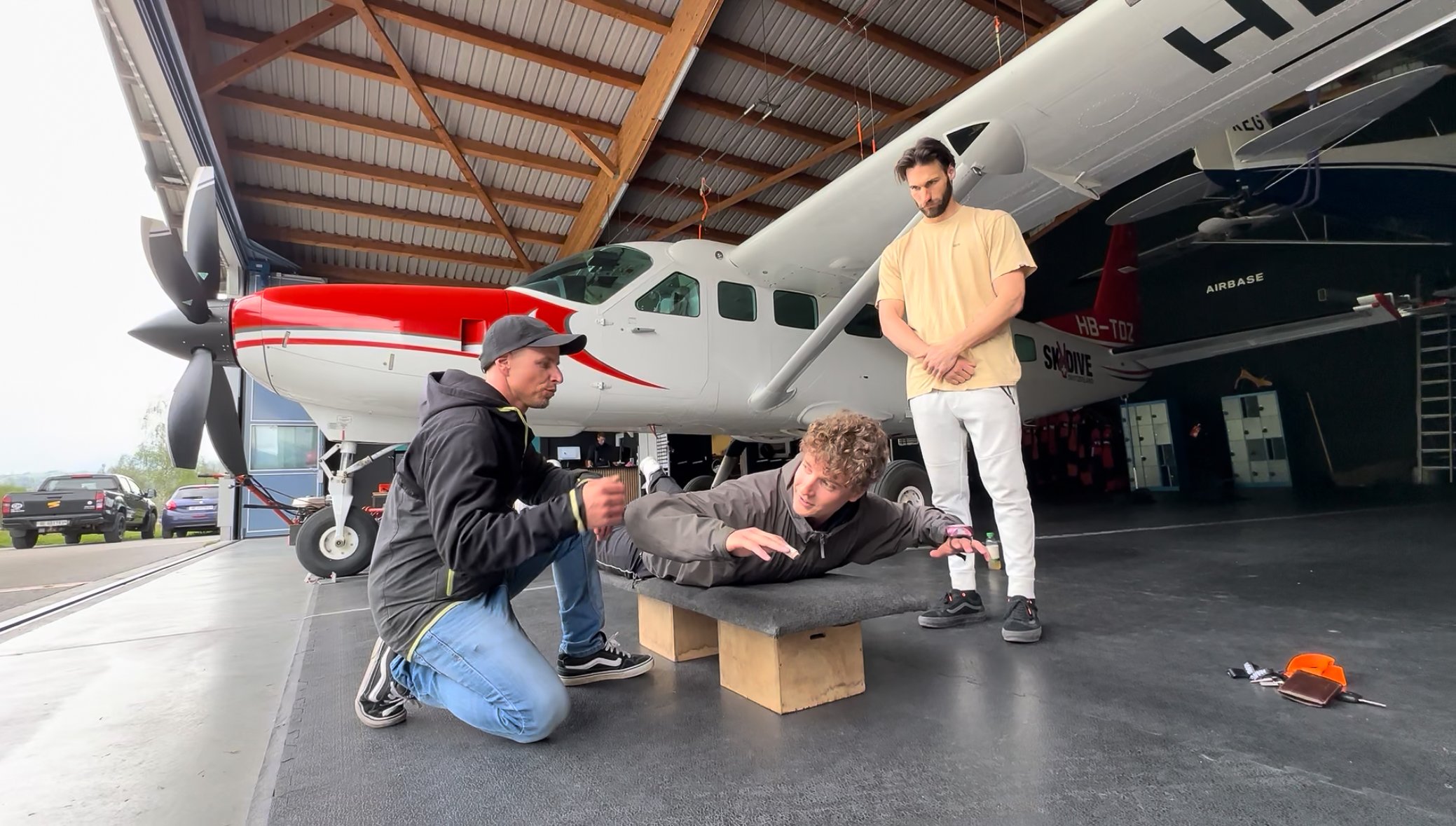 People are practicing skydiving techniques in a hangar next to an airplane.