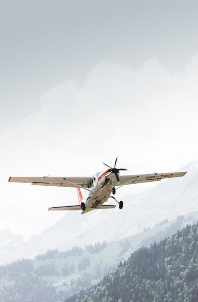 Kleinflugzeug fliegt über bewaldete Berge in der Schweiz.